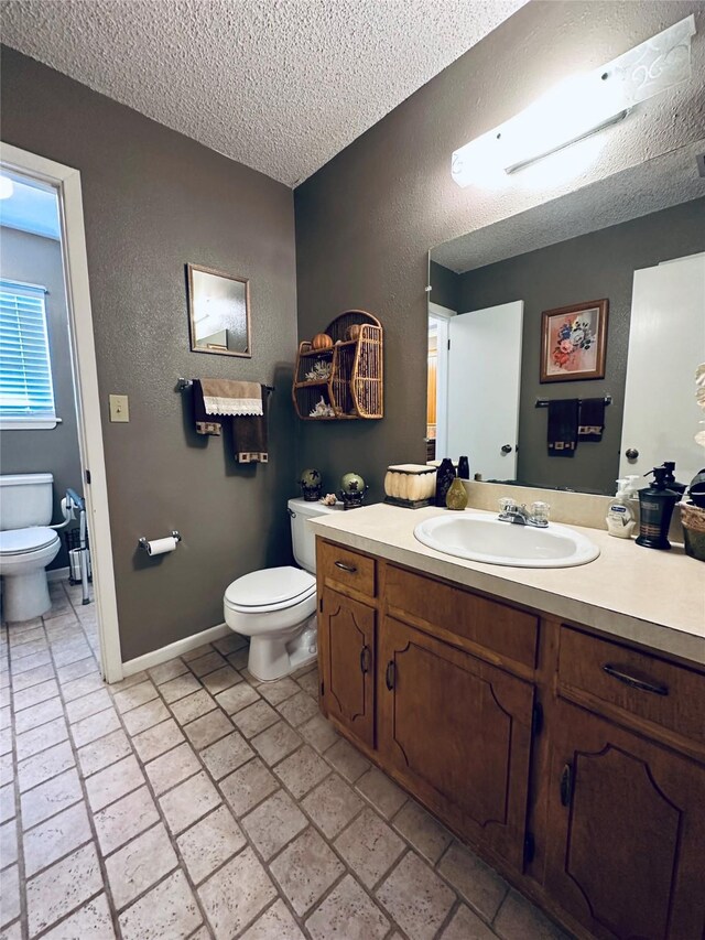 1402 Marie St N, Comanche, TX 76442 - bathroom featuring toilet, a textured ceiling, vanity, a textured wall, and baseboards