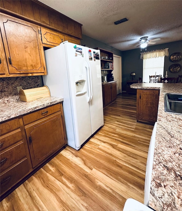 1402 Marie St N, Comanche, TX 76442 - kitchen featuring white fridge with ice dispenser, light wood-type flooring, a textured ceiling, a ceiling fan, and brown cabinetry