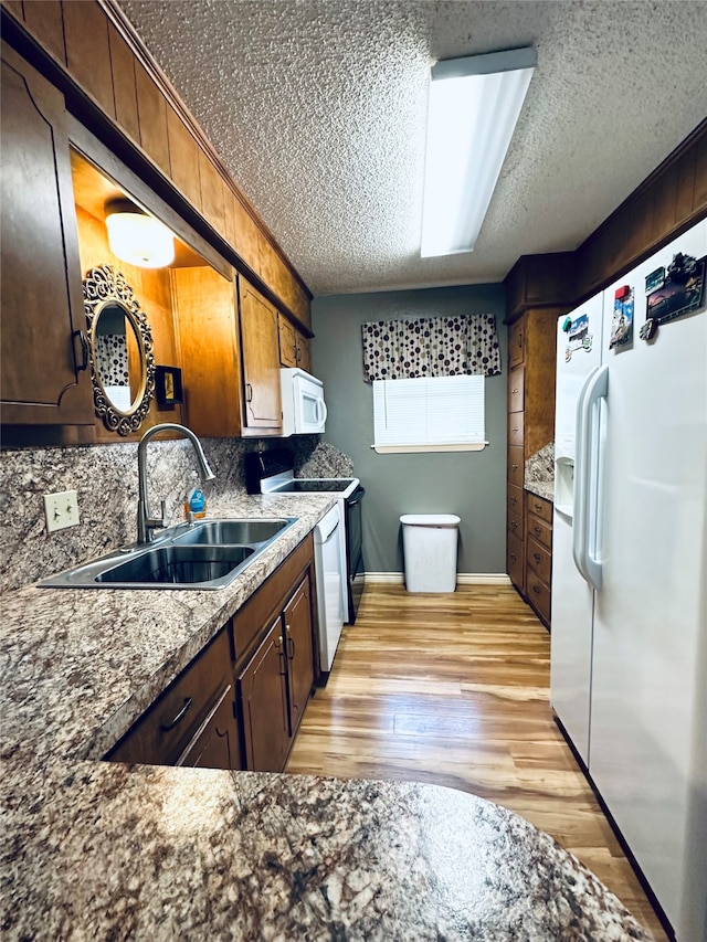 kitchen featuring sink, white appliances, a textured ceiling, light hardwood / wood-style flooring, and backsplash