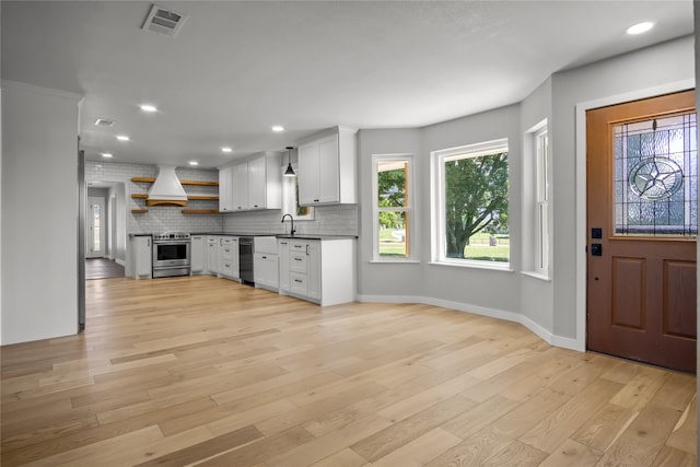 kitchen with white cabinets, custom exhaust hood, stainless steel range with electric cooktop, black dishwasher, and light hardwood / wood-style floors