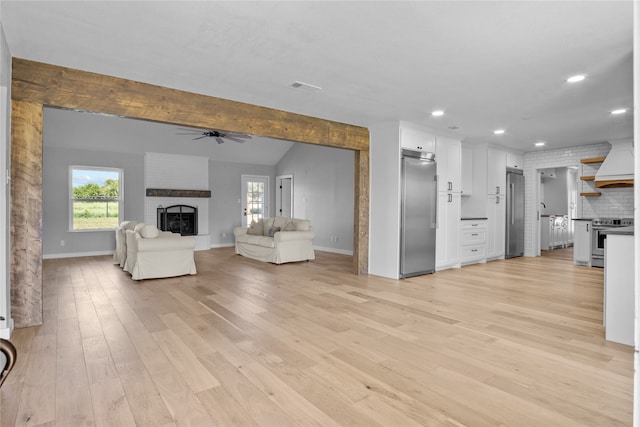 unfurnished living room featuring vaulted ceiling with beams, ceiling fan, light hardwood / wood-style flooring, and a brick fireplace