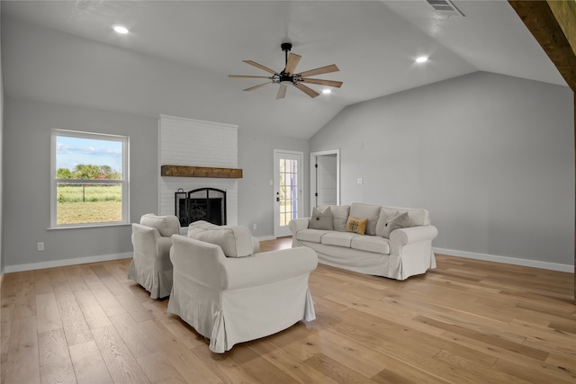 living room with light wood-type flooring, lofted ceiling, ceiling fan, and a brick fireplace