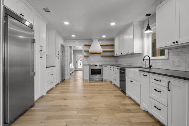 kitchen featuring stainless steel appliances, light hardwood / wood-style floors, hanging light fixtures, and custom range hood