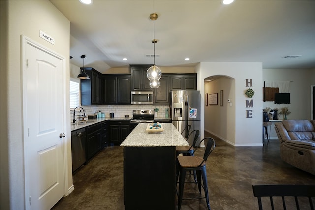 kitchen with appliances with stainless steel finishes, hanging light fixtures, tasteful backsplash, a kitchen bar, and a center island