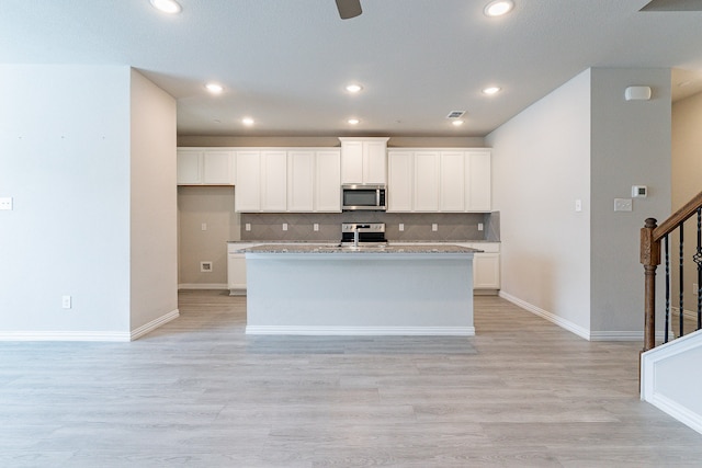 kitchen with light wood-type flooring, light stone counters, white cabinetry, a center island with sink, and appliances with stainless steel finishes