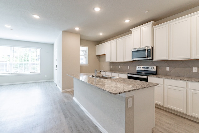 kitchen featuring a kitchen island with sink, stainless steel appliances, light wood-type flooring, and sink