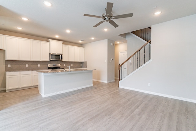 kitchen featuring ceiling fan, white cabinets, a center island with sink, appliances with stainless steel finishes, and light wood-type flooring