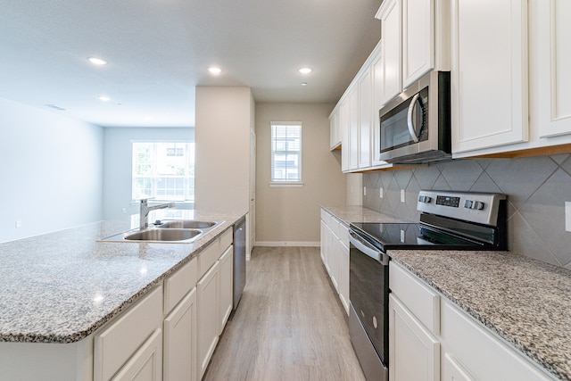 kitchen with sink, white cabinetry, light hardwood / wood-style flooring, stainless steel appliances, and a center island with sink