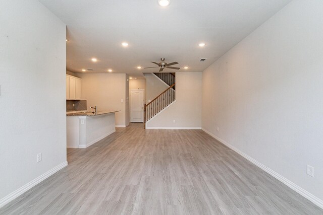 unfurnished living room featuring light wood-type flooring, ceiling fan, and sink