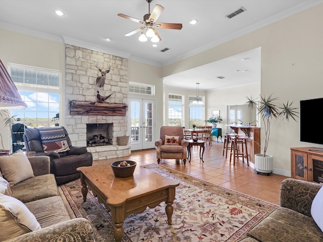 living room with ceiling fan, a stone fireplace, ornamental molding, and light tile patterned floors