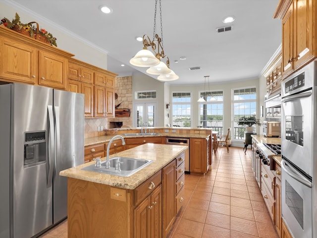 kitchen featuring an island with sink, kitchen peninsula, stainless steel appliances, a healthy amount of sunlight, and decorative light fixtures