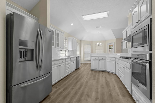 kitchen featuring appliances with stainless steel finishes, white cabinets, kitchen peninsula, an inviting chandelier, and light hardwood / wood-style flooring