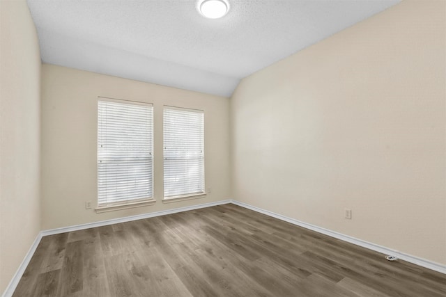 spare room featuring wood-type flooring, a textured ceiling, and lofted ceiling