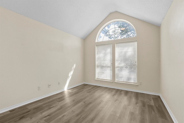 spare room with wood-type flooring, vaulted ceiling, and a textured ceiling