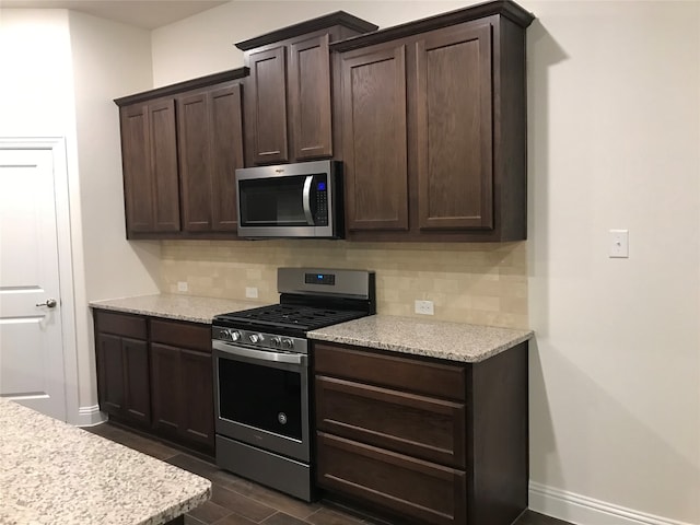 kitchen featuring decorative backsplash, dark wood-type flooring, light stone counters, stainless steel appliances, and dark brown cabinets