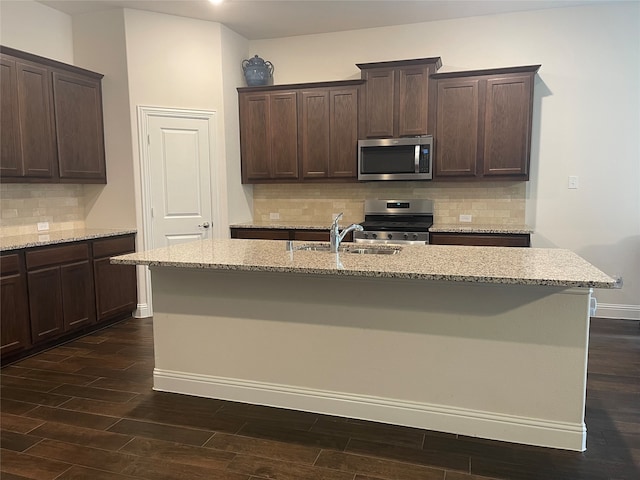 kitchen with sink, a center island with sink, backsplash, appliances with stainless steel finishes, and dark hardwood / wood-style floors