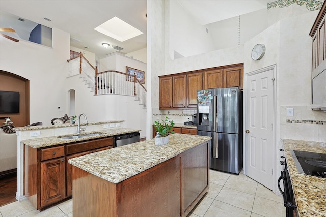 kitchen with appliances with stainless steel finishes, a towering ceiling, a center island, ceiling fan, and sink