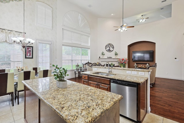 kitchen featuring an island with sink, ceiling fan with notable chandelier, a high ceiling, stainless steel dishwasher, and sink