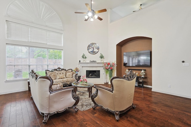 living room with a high ceiling, ceiling fan, a fireplace, and dark hardwood / wood-style flooring