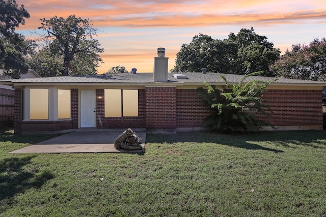 back house at dusk with a lawn and a patio area