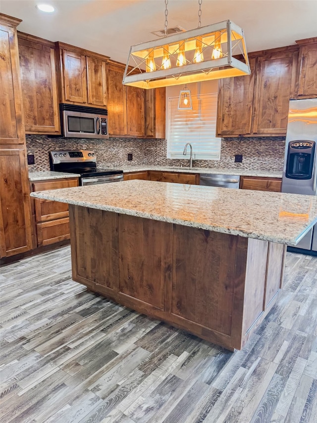 kitchen with light stone counters, pendant lighting, stainless steel appliances, a center island, and light hardwood / wood-style flooring