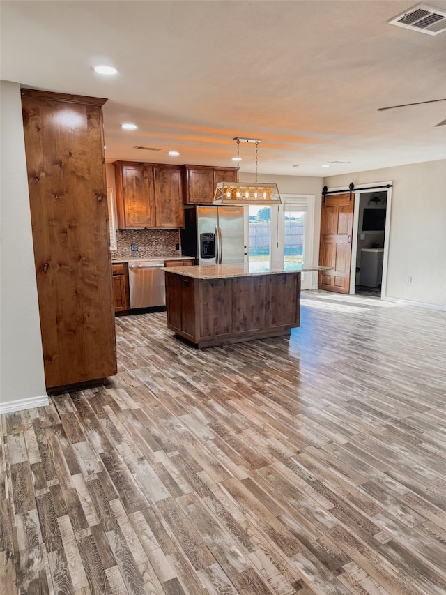 kitchen with pendant lighting, stainless steel appliances, hardwood / wood-style flooring, and a barn door