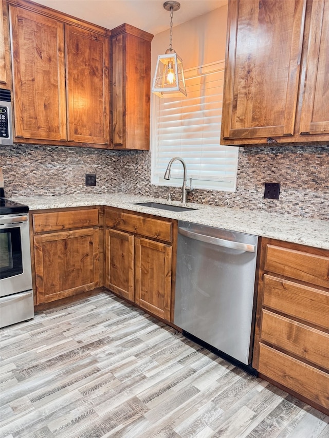 kitchen featuring hanging light fixtures, sink, tasteful backsplash, light hardwood / wood-style flooring, and appliances with stainless steel finishes