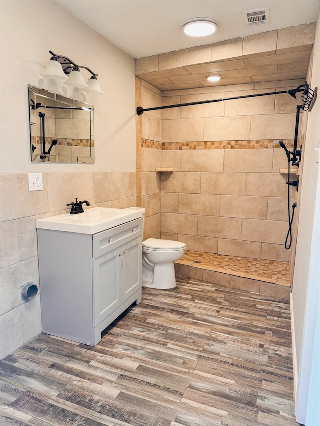 bathroom with a tile shower, vanity, toilet, and hardwood / wood-style flooring