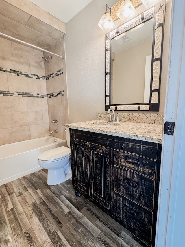 full bathroom with hardwood / wood-style floors, tiled shower / bath combo, vanity, and toilet