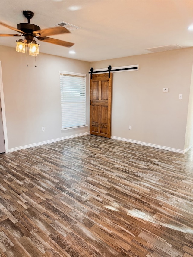 spare room featuring ceiling fan, dark wood-type flooring, and a barn door