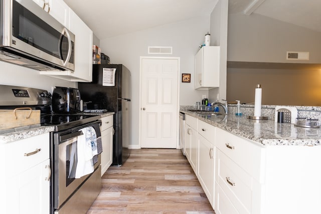 kitchen with white cabinets, lofted ceiling, appliances with stainless steel finishes, and light stone counters