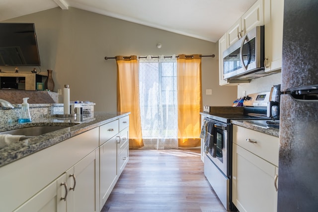 kitchen featuring white cabinets, vaulted ceiling with beams, stainless steel appliances, dark stone countertops, and light hardwood / wood-style floors