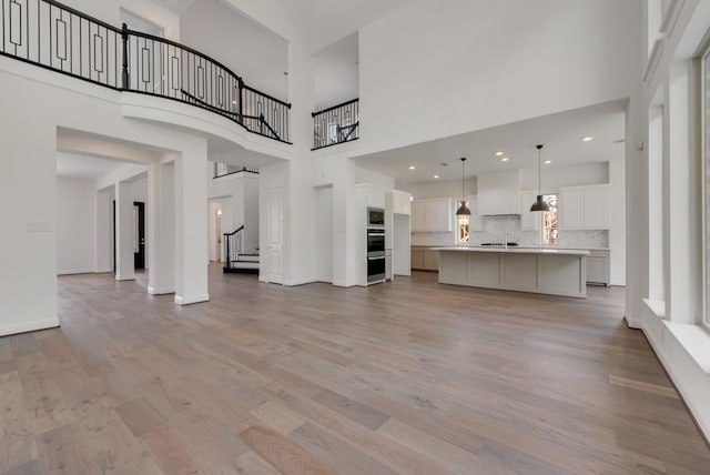 unfurnished living room with stairs, a high ceiling, light wood-type flooring, and baseboards