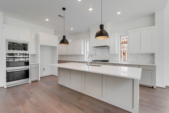 kitchen featuring light wood finished floors, backsplash, a sink, and visible vents