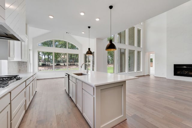 kitchen with light countertops, stainless steel gas stovetop, a premium fireplace, a sink, and wall chimney exhaust hood