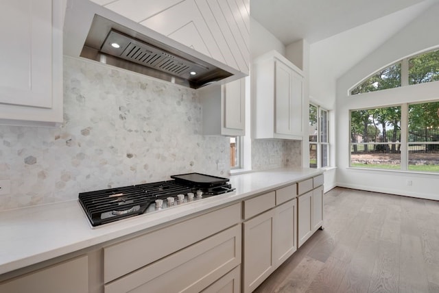 kitchen with light countertops, custom range hood, stainless steel gas stovetop, backsplash, and light wood-type flooring