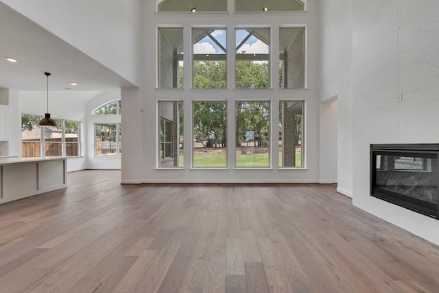 unfurnished living room with light wood-type flooring, a fireplace, a towering ceiling, and baseboards