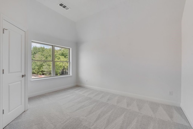 spare room with light carpet, baseboards, visible vents, and vaulted ceiling