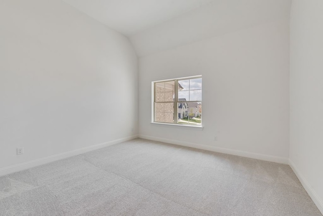 spare room featuring light carpet, vaulted ceiling, and baseboards