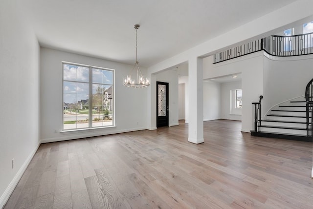 unfurnished dining area with baseboards, light wood finished floors, stairway, and a notable chandelier