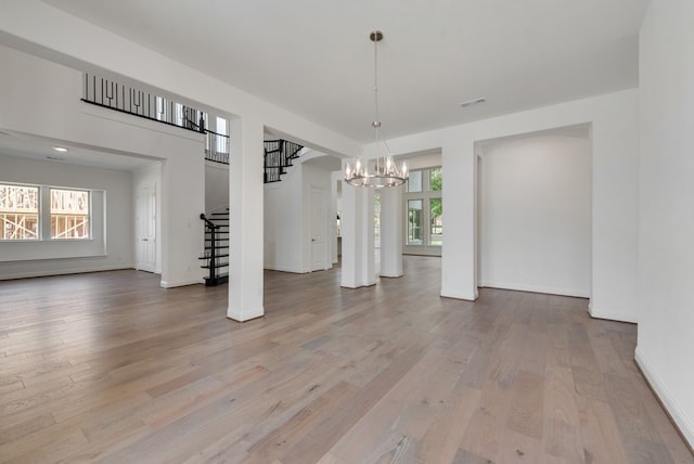 unfurnished dining area with visible vents, baseboards, stairway, light wood-type flooring, and a chandelier