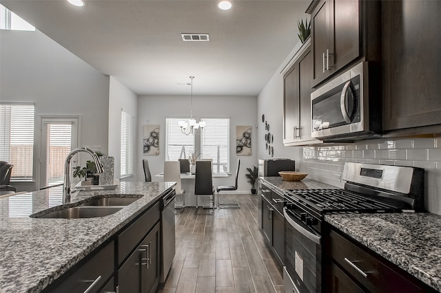 kitchen with appliances with stainless steel finishes, light stone counters, an inviting chandelier, dark brown cabinetry, and sink