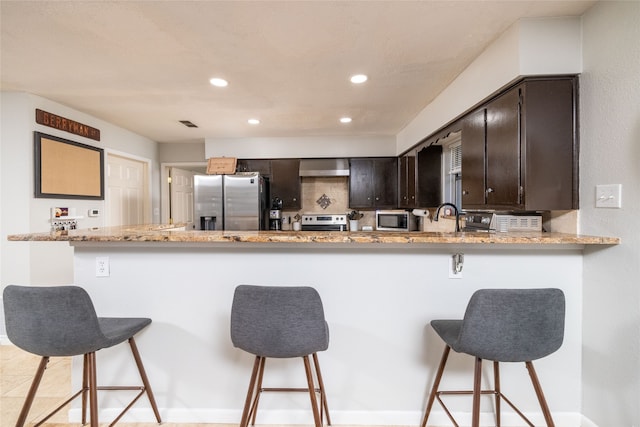 kitchen with kitchen peninsula, dark brown cabinetry, sink, a breakfast bar area, and appliances with stainless steel finishes