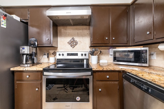 kitchen featuring light stone counters, tasteful backsplash, wall chimney range hood, dark brown cabinets, and appliances with stainless steel finishes