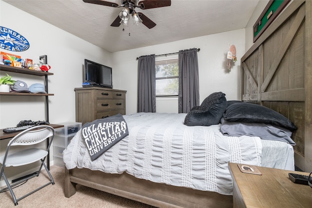 bedroom featuring a textured ceiling, light colored carpet, a barn door, and ceiling fan