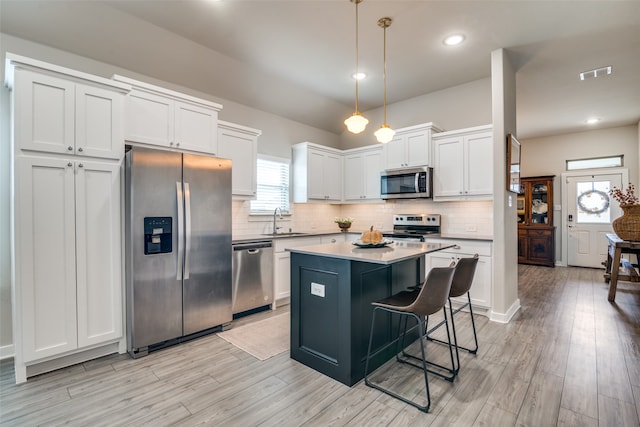 kitchen with white cabinets, pendant lighting, stainless steel appliances, a center island, and light hardwood / wood-style flooring