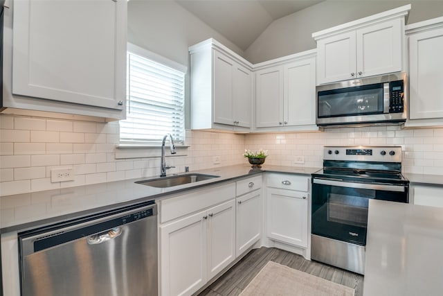 kitchen with white cabinets, sink, stainless steel appliances, vaulted ceiling, and decorative backsplash