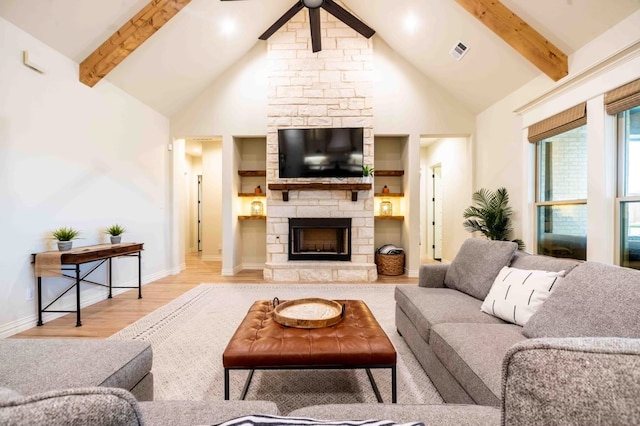 living room with high vaulted ceiling, a stone fireplace, light hardwood / wood-style floors, and beamed ceiling