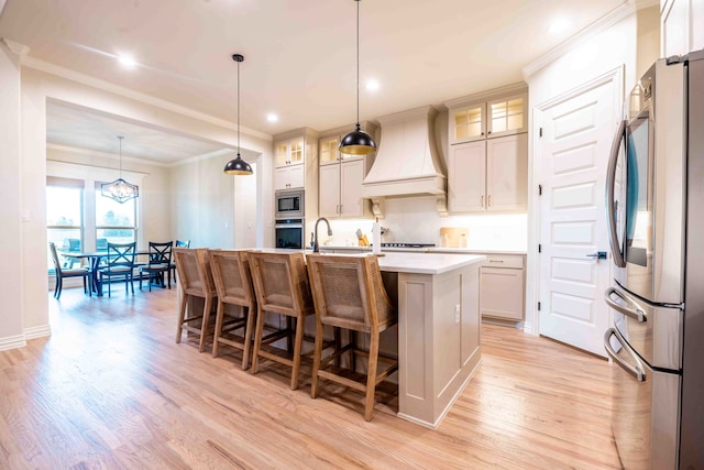 kitchen featuring custom exhaust hood, appliances with stainless steel finishes, a kitchen island with sink, and hanging light fixtures