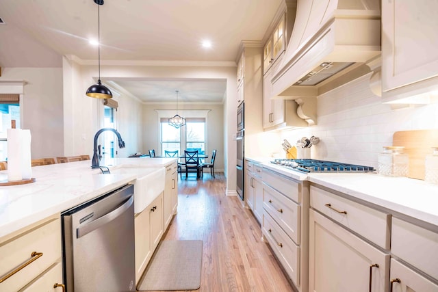 kitchen with appliances with stainless steel finishes, sink, decorative backsplash, hanging light fixtures, and light hardwood / wood-style floors